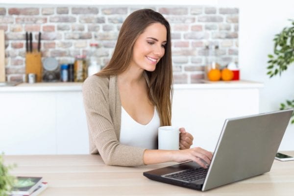 beautiful-young-woman-using-her-laptop-kitchen_1301-7666